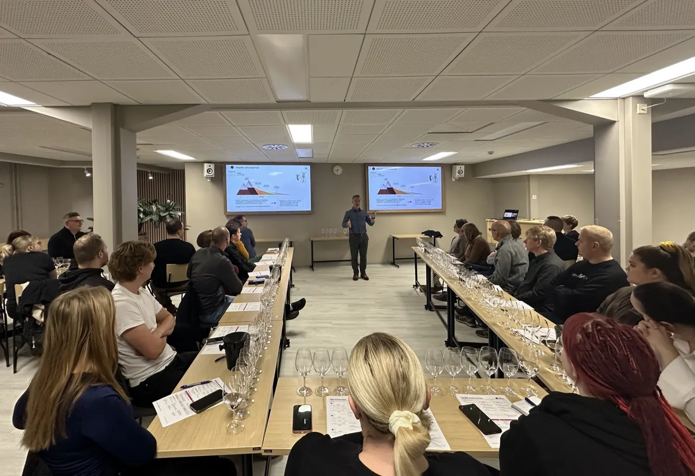 The masterclass room at JAMK: tasters seated along long tables with glasses and tasting sheets, Luciano presenting at the front